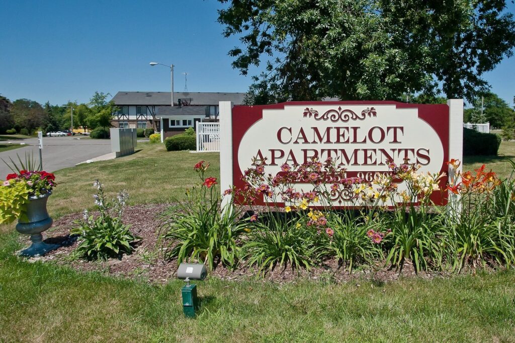 A sign in front of a building that says " camelot apartments ".